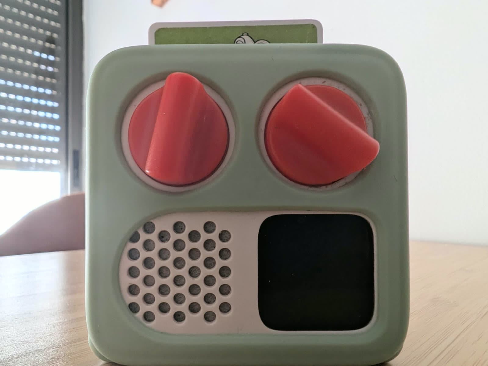 A Yoto Mini in a mint silicone case on a wooden table, a card sticking out of the top